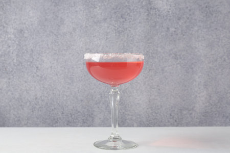 Martini cocktail with sugar in glass on white table near grey wall, closeup