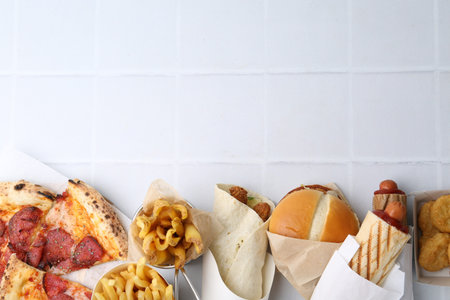 Different delicious fast food on white tiled table, flat lay. Space for text