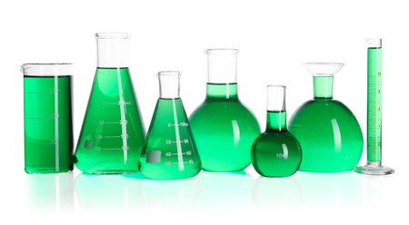Different laboratory glassware with green liquid on mirror surface isolated on whiteの写真素材
