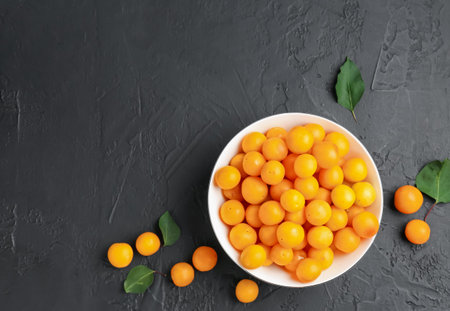 Ripe yellow cherry plums and leaves on black table, flat lay. Space for textの写真素材