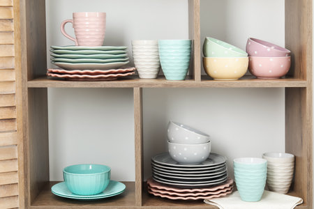 Shelving unit with different dishware and cups near white wall indoorsの写真素材