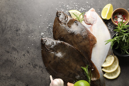 Fresh flounder fish, spices and products on gray textured table, flat lay with space for text. Raw...