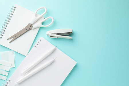 White notebooks and other stationery on light blue background, flat lay. Space for text