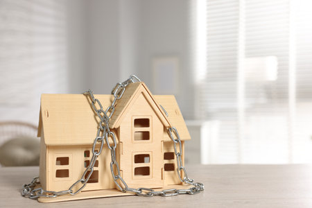 Home security. House model with chain on wooden table indoors, space for textの写真素材