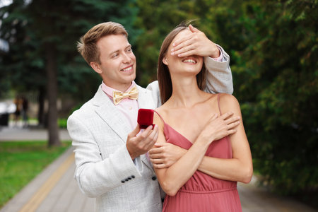Making marriage proposal. Smiling man with engagement ring surprising his girlfriend outdoorsの写真素材