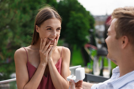 Man with engagement ring making marriage proposal to his happy girlfriend outdoorsの写真素材