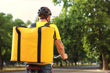 Courier with thermo bag riding bicycle outdoors, back view. Food delivery serviceの写真素材