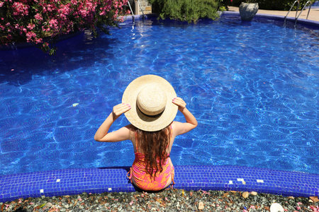 Girl in straw hat at poolside outdoors on sunny day, back view