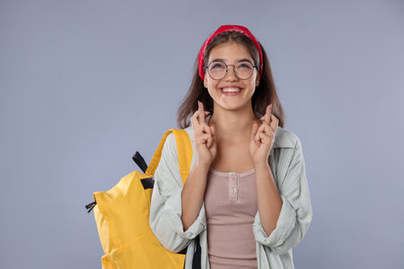 Excited student crossing fingers on gray background. Hope for good exam resultの写真素材