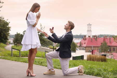 Smiling man with engagement ring making marriage proposal to his surprised girlfriend outdoors