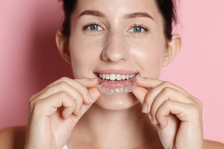 Beautiful woman wearing dental aligner on pink background, closeup