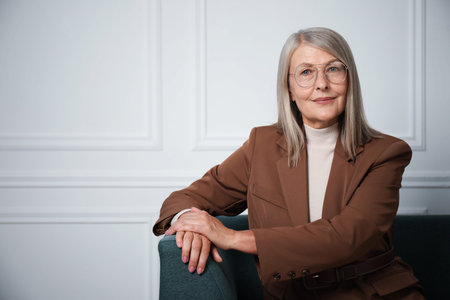 Portrait of beautiful senior woman on sofa near white wall. Space for text