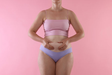 Woman in underwear touching her belly on pink background, closeupの写真素材