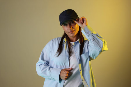 Portrait of beautiful woman wearing baseball cap in neon lights against color background