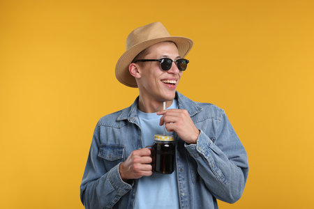 Happy man in sunglasses and hat with mason jar of refreshing soda drink on yellow backgroundの写真素材
