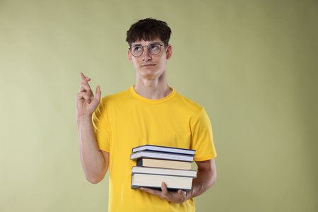 Worried student crossing fingers for good exam result on light olive backgroundの写真素材