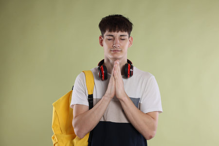 Student with clasped hands praying for good exam result on light olive background