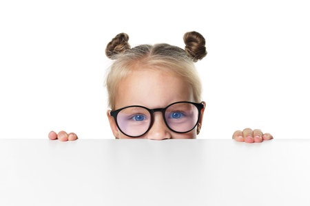 Curious little girl in glasses peeking over table against white backgroundの写真素材