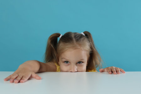 Curious little girl peeking over white table against light blue backgroundの写真素材
