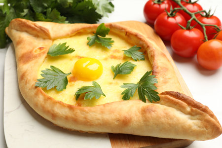 Tasty khachapuri with cheese, egg, parsley and tomatoes on white table, closeupの写真素材