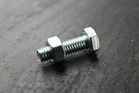 Metal bolt and nut on black table, closeup