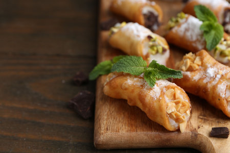 Delicious cannoli with cheese, nuts, chocolate, mint and powdered sugar on wooden table, closeup....