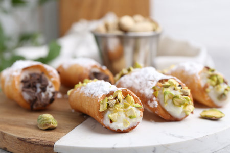 Delicious cannoli with ricotta cheese, pistachios, chocolate and powdered sugar on table against blurred background, closeupの写真素材