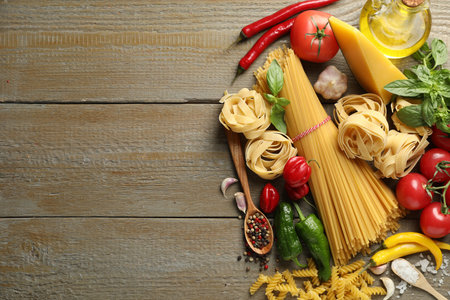 Different types of pasta and ingredients on wooden table, flat lay. Space for textの写真素材