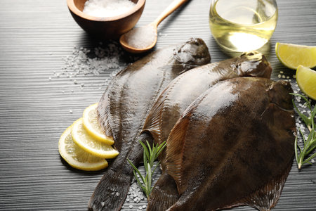 Fresh flounder fish, salt and products on black wooden table, closeup. Raw seafood