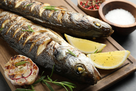 Tasty roasted seabass fish served with rosemary and lemon on gray table, closeup. Homemade seafood dishの写真素材