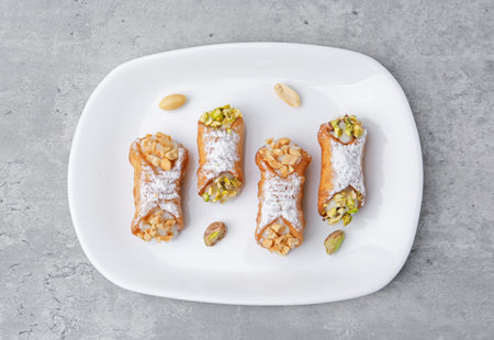 Delicious cannoli with ricotta cheese, peanuts, pistachios and powdered sugar on gray textured table, top viewの写真素材