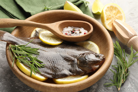 Fresh raw flounder fish, spices and wooden juicer on gray table, closeup. Seafood