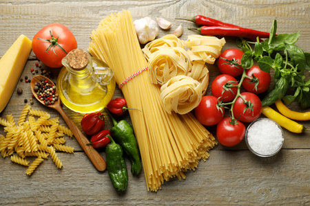 Different types of pasta and ingredients on wooden table, flat layの写真素材