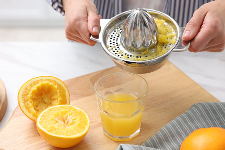 Woman pouring freshly squeezed orange juice into glass at white marble table indoors, closeup