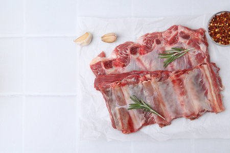 Fresh raw beef ribs and spices on white tiled table, flat lay. Space for text