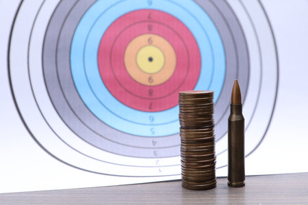 Firearm cartridge, stack of coins on table against targetの写真素材
