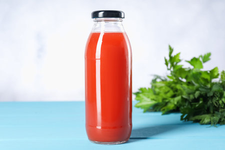 Tasty juice in glass bottle and parsley on light blue wooden table, closeup