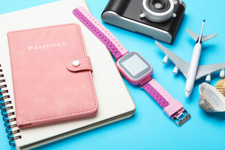 Time for summer vacation. Passport, notebook, toy plane, camera, smart watch and seashells on light blue background, closeupの写真素材