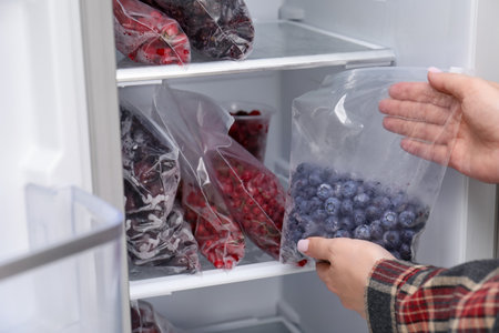 Freezing berries. Woman putting plastic bag with blueberries into open refrigerator, closeupの写真素材