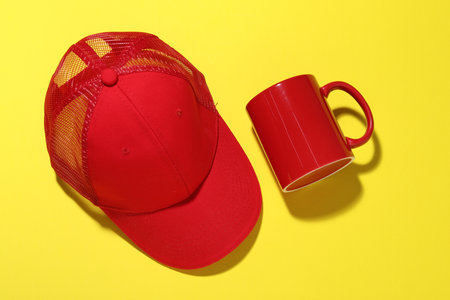 Red mug and cap on yellow background, flat lay. Mockup for designの写真素材