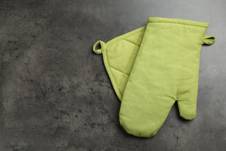 Green oven glove and potholder on dark textured table, top view. Space for textの写真素材