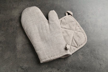 Gray oven glove and potholder on dark textured table, top viewの写真素材