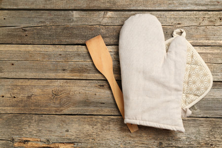 Oven glove, potholder and spatula on wooden table, flat lay. Space for textの写真素材