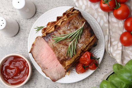 Delicious baked beef meat, tomatoes, basil, rosemary and sauce on grey table, flat layの写真素材