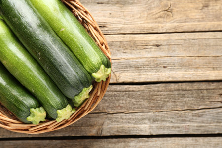 Fresh ripe zucchinis in wicker basket on wooden table, top view. Space for textの写真素材
