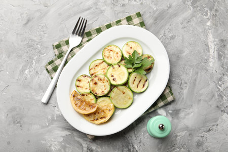 Delicious fried courgette slices with lemon and parsley served on grey table, flat layの写真素材