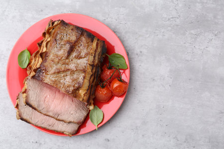 Delicious baked beef meat, tomatoes and basil on grey table, top view. Space for text