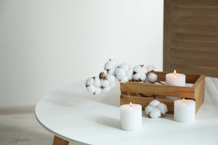 Crate with burning candles and cotton flowers on white table at homeの写真素材
