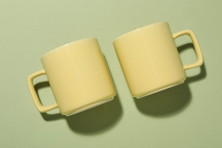 Yellow mugs on light green background, top view. Mockup for designの写真素材