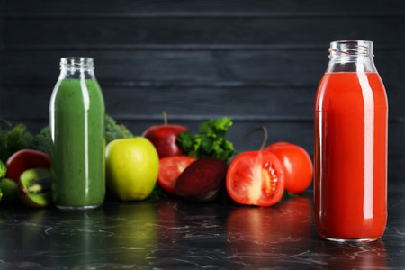 Tasty juices in glass bottles and ingredients on black marble tableの写真素材
